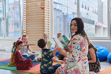 Image showing Reading time in an elementary school or kindergarten, a teacher reading a book to children in an elementary school or kindergarten. The concept of pre-school education. Selective focus