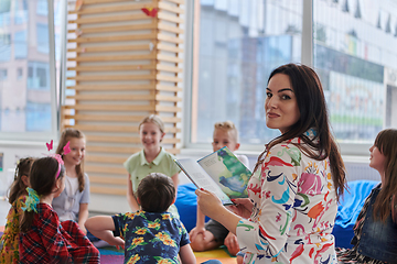 Image showing Reading time in an elementary school or kindergarten, a teacher reading a book to children in an elementary school or kindergarten. The concept of pre-school education. Selective focus