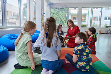 Image showing Reading time in an elementary school or kindergarten, a teacher reading a book to children in an elementary school or kindergarten. The concept of pre-school education. Selective focus