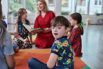 Image showing Reading time in an elementary school or kindergarten, a teacher reading a book to children in an elementary school or kindergarten. The concept of pre-school education. Selective focus