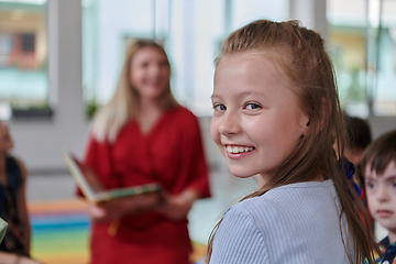 Image showing Reading time in an elementary school or kindergarten, a teacher reading a book to children in an elementary school or kindergarten. The concept of pre-school education. Selective focus