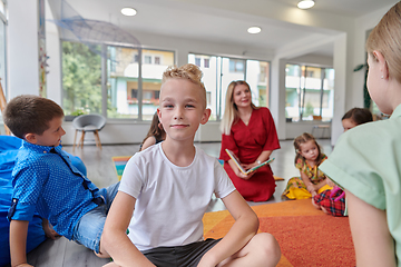 Image showing Reading time in an elementary school or kindergarten, a teacher reading a book to children in an elementary school or kindergarten. The concept of pre-school education. Selective focus