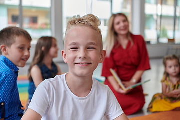 Image showing Reading time in an elementary school or kindergarten, a teacher reading a book to children in an elementary school or kindergarten. The concept of pre-school education. Selective focus