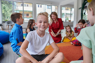 Image showing Reading time in an elementary school or kindergarten, a teacher reading a book to children in an elementary school or kindergarten. The concept of pre-school education. Selective focus