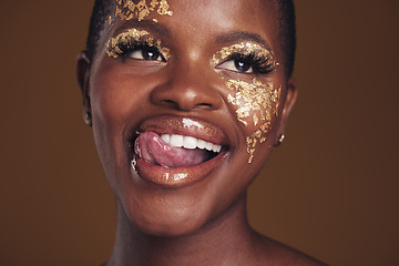 Image showing Gold, glitter and black woman beauty with makeup and tongue out in studio with sparkle cosmetics. Brown background, funny and female model with golden paint for skin glow and creative facial shine