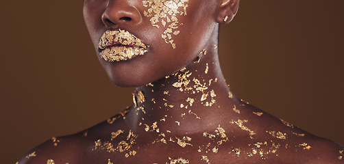 Image showing Beauty, lips and black woman with gold makeup on brown background for art, cosmetics and glitter paint. Shine, glow and zoom on model mouth for aesthetic luxury, skincare and metal lipstick in studio