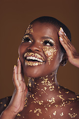 Image showing Gold, glitter flake and black woman beauty with makeup and luxury in studio with sparkle cosmetics. Brown background, smile and female model with golden paint for skin glow and creative facial shine