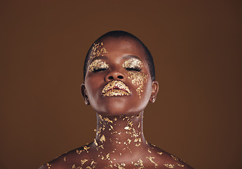 Image showing Beauty, glitter and black woman with gold makeup on brown background with art, paint and cosmetics. Shine, glow and African model in studio for facial fashion, aesthetic freedom and luxury skincare.