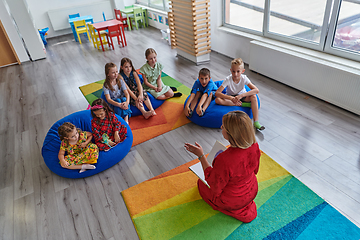 Image showing A happy female teacher sitting and playing hand games with a group of little schoolchildren