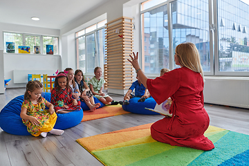 Image showing A happy female teacher sitting and playing hand games with a group of little schoolchildren