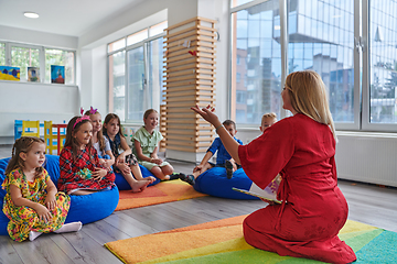 Image showing A happy female teacher sitting and playing hand games with a group of little schoolchildren