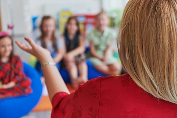 Image showing A happy female teacher sitting and playing hand games with a group of little schoolchildren