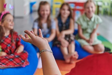 Image showing A happy female teacher sitting and playing hand games with a group of little schoolchildren