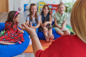 Image showing A happy female teacher sitting and playing hand games with a group of little schoolchildren