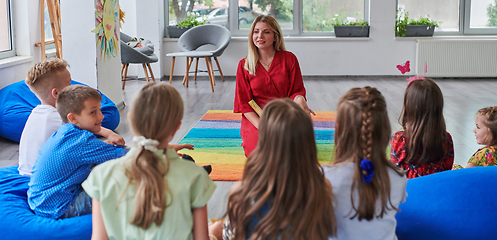 Image showing Reading time in an elementary school or kindergarten, a teacher reading a book to children in an elementary school or kindergarten. The concept of pre-school education. Selective focus