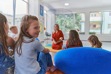 Image showing Reading time in an elementary school or kindergarten, a teacher reading a book to children in an elementary school or kindergarten. The concept of pre-school education. Selective focus