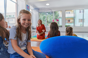 Image showing Reading time in an elementary school or kindergarten, a teacher reading a book to children in an elementary school or kindergarten. The concept of pre-school education. Selective focus