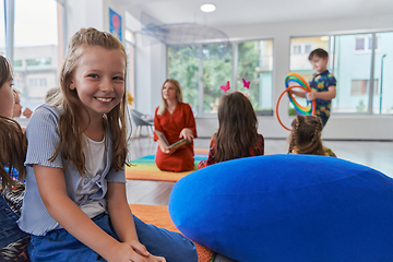 Image showing Reading time in an elementary school or kindergarten, a teacher reading a book to children in an elementary school or kindergarten. The concept of pre-school education. Selective focus