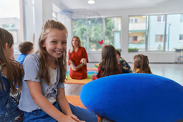 Image showing Reading time in an elementary school or kindergarten, a teacher reading a book to children in an elementary school or kindergarten. The concept of pre-school education. Selective focus