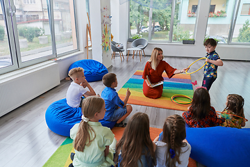 Image showing A happy female teacher sitting and playing hand games with a group of little schoolchildren