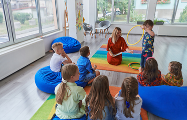 Image showing A happy female teacher sitting and playing hand games with a group of little schoolchildren