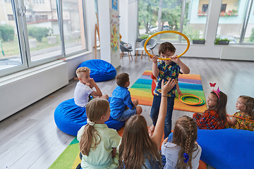 Image showing A happy female teacher sitting and playing hand games with a group of little schoolchildren