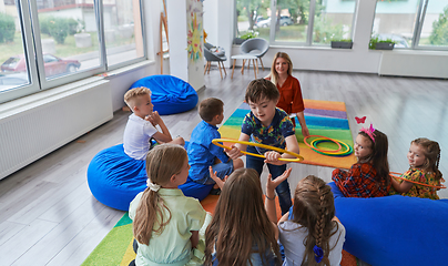 Image showing A happy female teacher sitting and playing hand games with a group of little schoolchildren