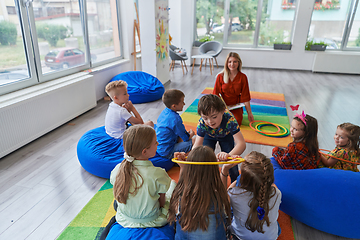 Image showing A happy female teacher sitting and playing hand games with a group of little schoolchildren