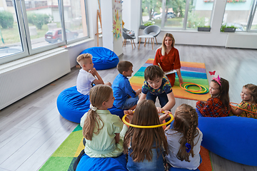 Image showing A happy female teacher sitting and playing hand games with a group of little schoolchildren