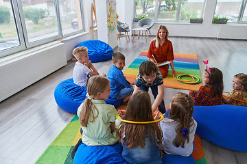 Image showing A happy female teacher sitting and playing hand games with a group of little schoolchildren