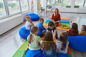 Image showing A happy female teacher sitting and playing hand games with a group of little schoolchildren