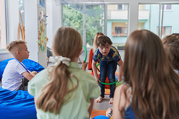 Image showing A happy female teacher sitting and playing hand games with a group of little schoolchildren