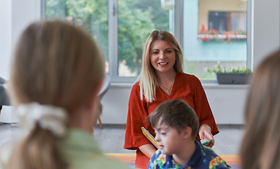 Image showing Reading time in an elementary school or kindergarten, a teacher reading a book to children in an elementary school or kindergarten. The concept of pre-school education. Selective focus