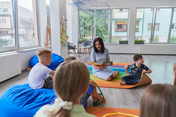 Image showing Reading time in an elementary school or kindergarten, a teacher reading a book to children in an elementary school or kindergarten. The concept of pre-school education. Selective focus