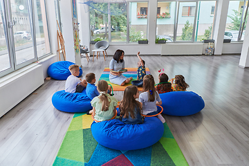 Image showing Reading time in an elementary school or kindergarten, a teacher reading a book to children in an elementary school or kindergarten. The concept of pre-school education. Selective focus