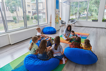 Image showing Reading time in an elementary school or kindergarten, a teacher reading a book to children in an elementary school or kindergarten. The concept of pre-school education. Selective focus