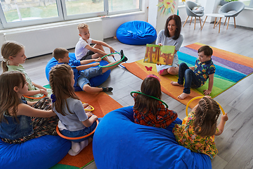 Image showing Reading time in an elementary school or kindergarten, a teacher reading a book to children in an elementary school or kindergarten. The concept of pre-school education. Selective focus