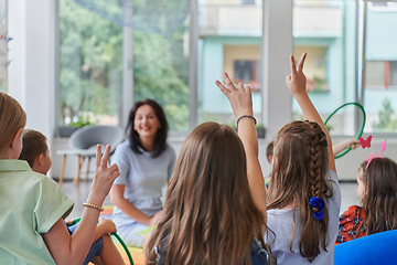 Image showing A happy female teacher sitting and playing hand games with a group of little schoolchildren