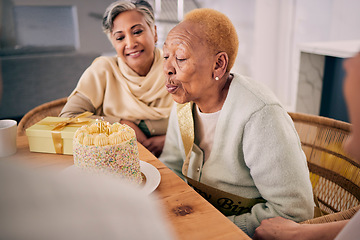 Image showing Senior woman blowing candles on her cake for birthday celebration at a house at a party with friends. Smile, happy and elderly female person with a dessert to celebrate with people in retirement home