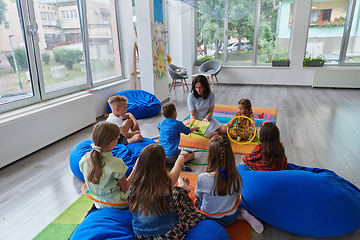 Image showing A happy female teacher sitting and playing hand games with a group of little schoolchildren