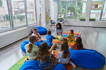 Image showing A happy female teacher sitting and playing hand games with a group of little schoolchildren