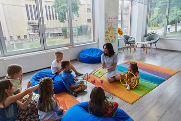 Image showing A happy female teacher sitting and playing hand games with a group of little schoolchildren