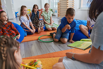 Image showing A happy female teacher sitting and playing hand games with a group of little schoolchildren