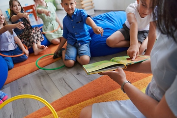 Image showing A happy female teacher sitting and playing hand games with a group of little schoolchildren