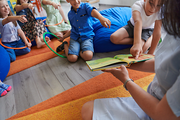 Image showing A happy female teacher sitting and playing hand games with a group of little schoolchildren