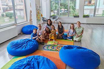 Image showing A happy female teacher sitting and playing hand games with a group of little schoolchildren