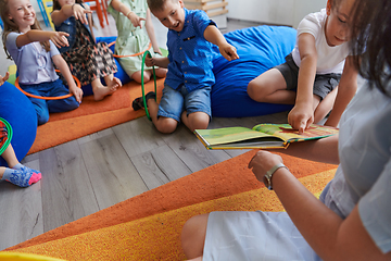 Image showing A happy female teacher sitting and playing hand games with a group of little schoolchildren