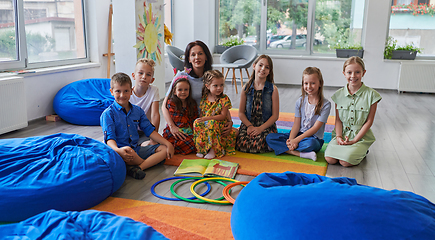 Image showing A happy female teacher sitting and playing hand games with a group of little schoolchildren