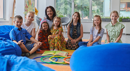 Image showing A happy female teacher sitting and playing hand games with a group of little schoolchildren