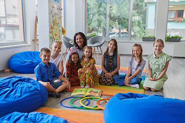 Image showing A happy female teacher sitting and playing hand games with a group of little schoolchildren